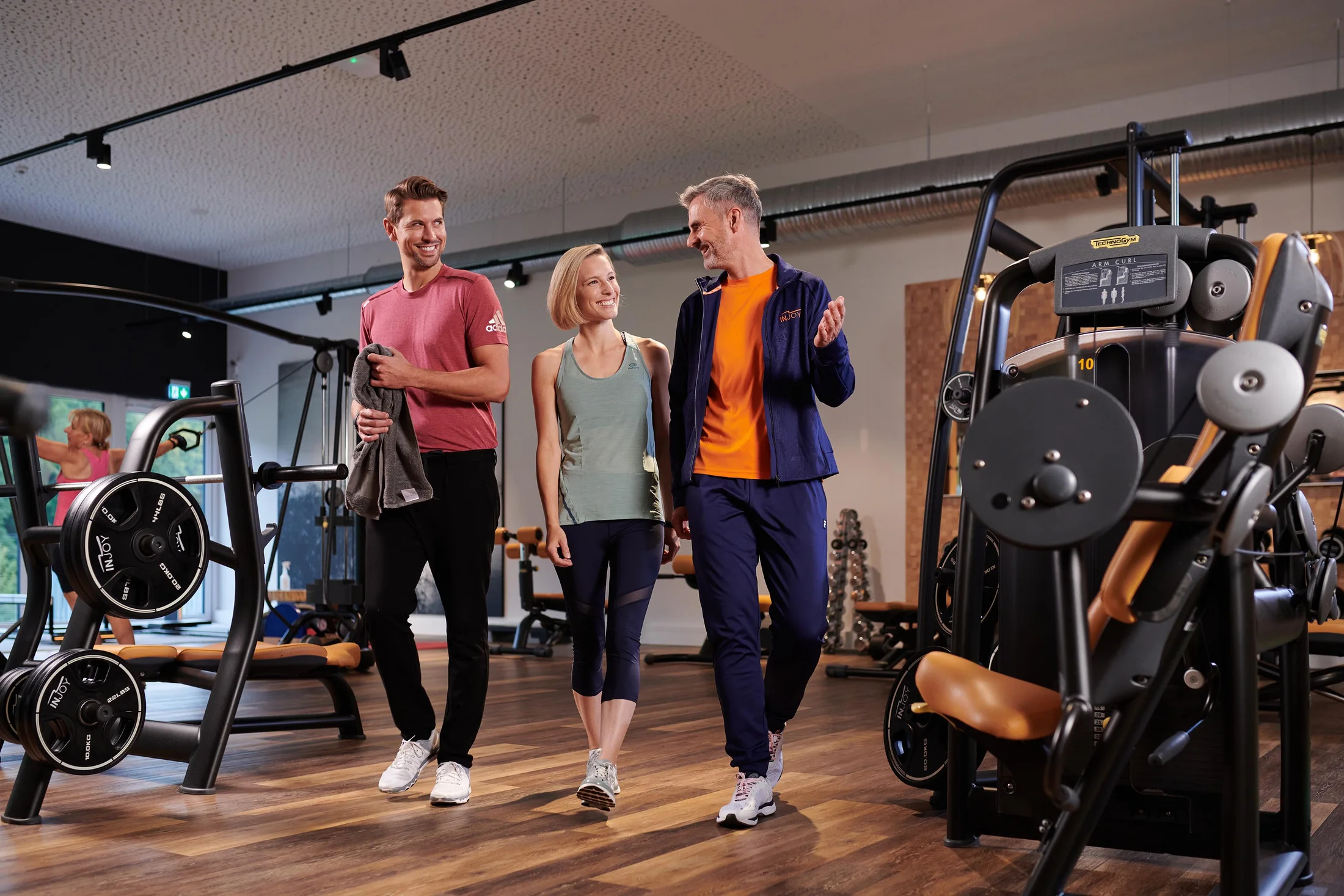 Mitglieder und Trainer gehen gemeinsam durch den modernen INJOY Trainingsbereich